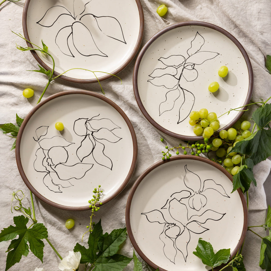 Four round ceramic dinner plates featuring Verve illustrations by Henri Matisse, styled with grapes and greenery.