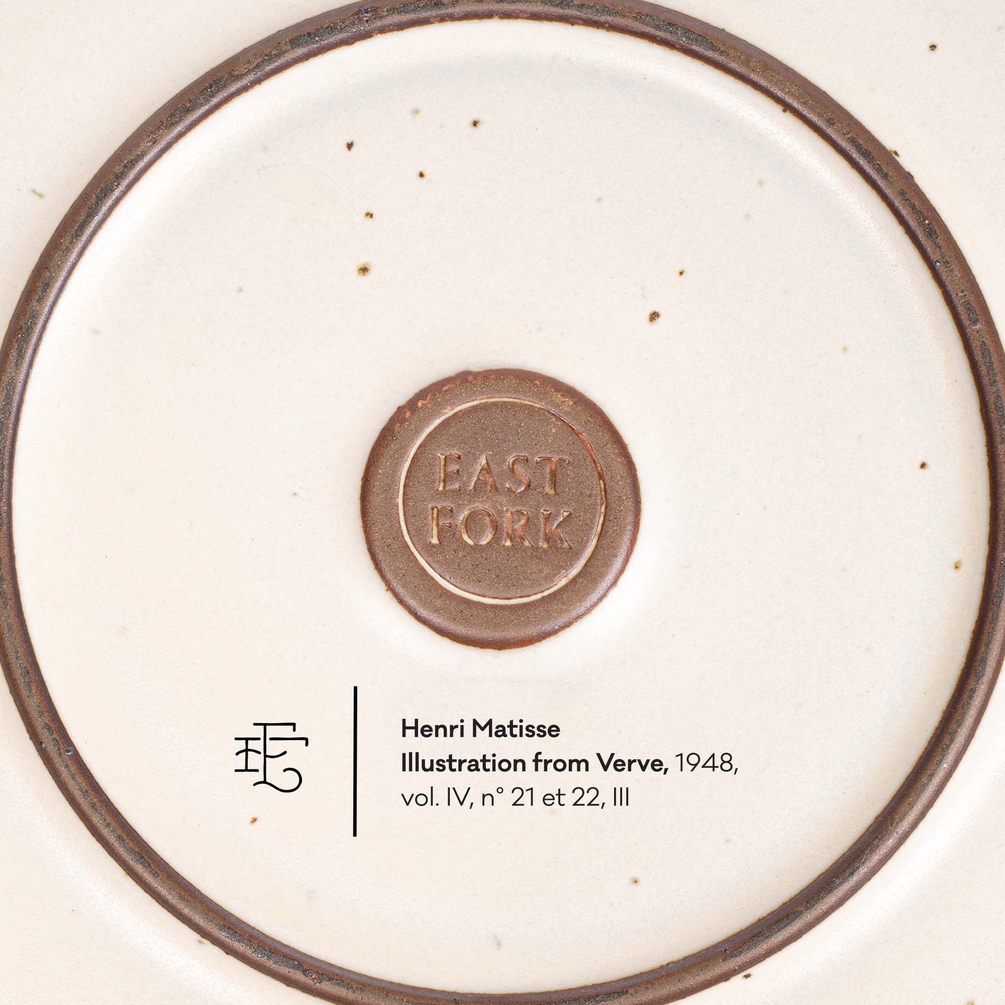 Close-up of the bottom of a white ceramic plate or dish with a brown rim and a central brown circular mark reading 'EAST FORK.' Small printed text below includes copyright and artist rights information.