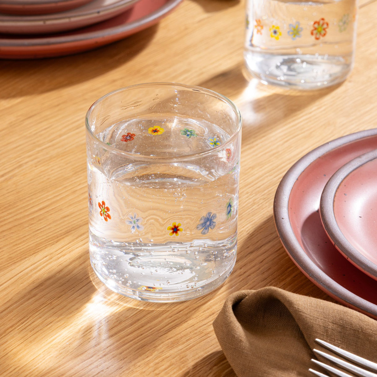 Clear glass with colorful flower pattern filled with sparkling water on a wooden table.