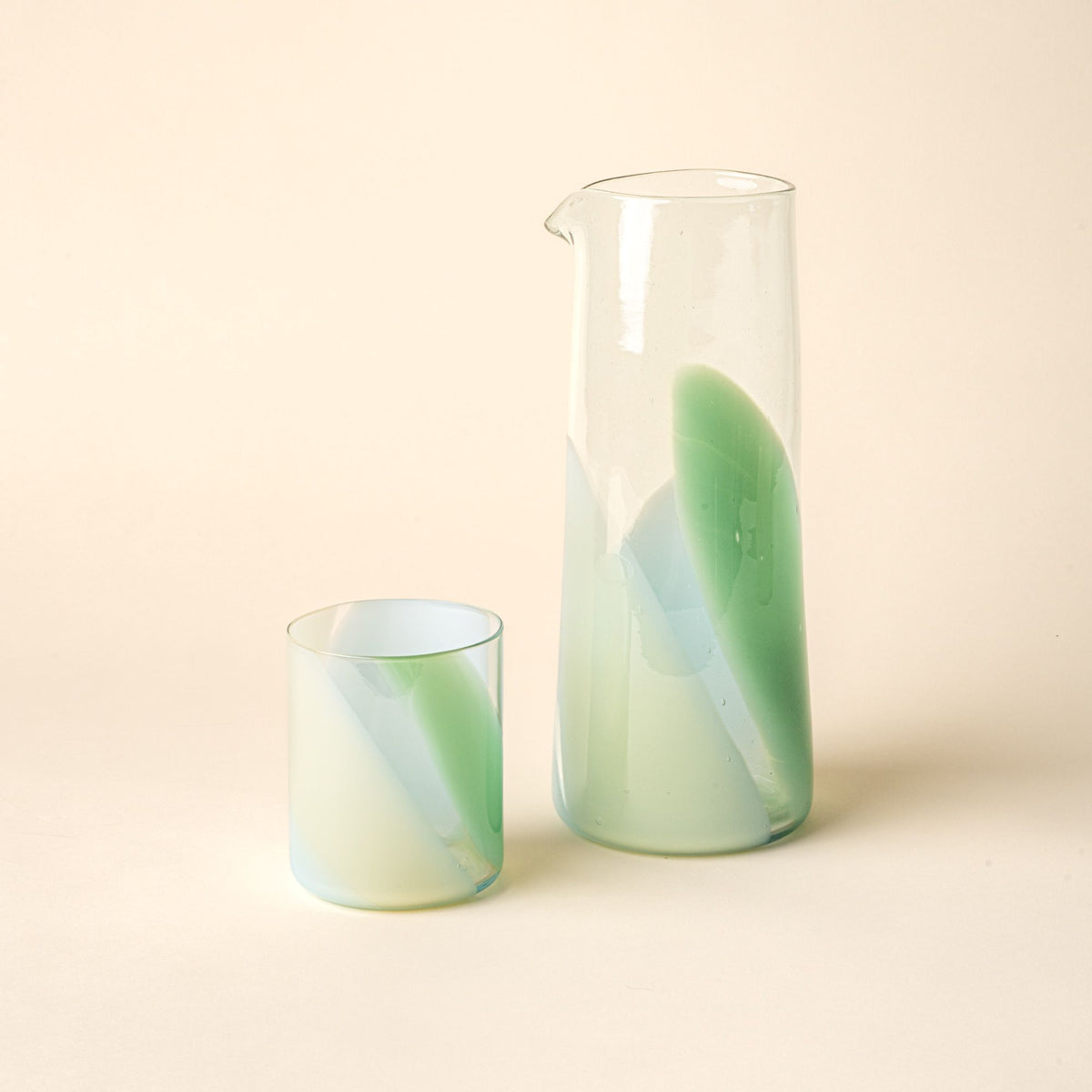 Hand-blown glass carafe and matching tumbler featuring a soft pastel green swirl design, displayed against a neutral background.