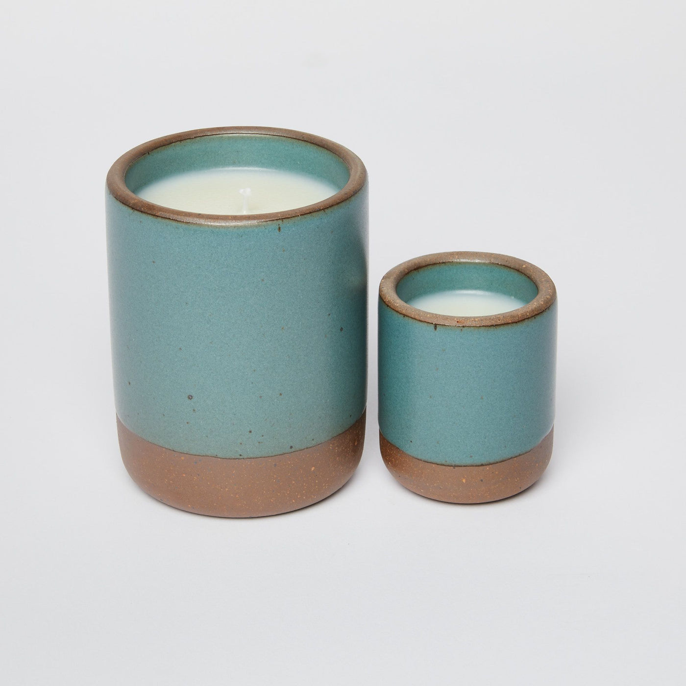 Two ceramic candles in a speckled teal glaze with a natural clay base, set against a plain white background.