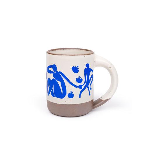 East Fork’s The Mug in a warm off white color with handle with a blue decal of Henri Matisse’s Femmes et singes, a bright blue, abstract cut-out figures of women sitting, monkeys, and pomegranate across the body of the mug