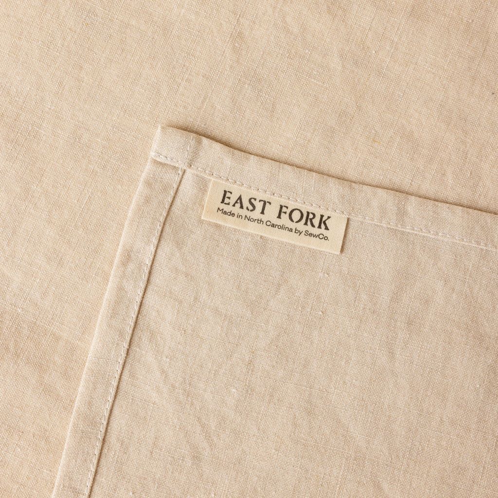 An off-white linen napkin close up of texture and sewn-in corner tag that reads "East Fork"