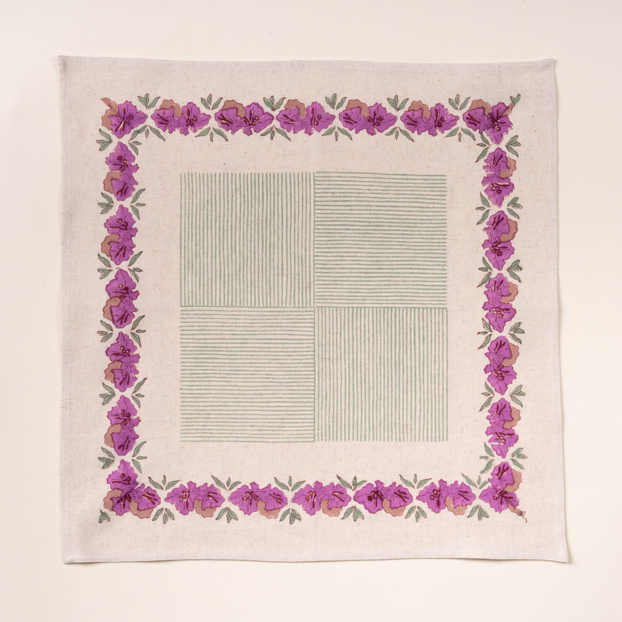 Square cotton napkin with a purple floral border and a pale green striped center design, laid flat on a cream background.