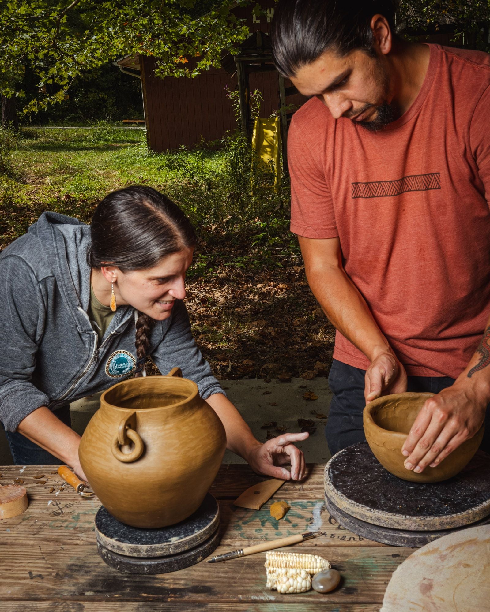 Two members of The Center for Native Health forming clay pots on a table outdoors