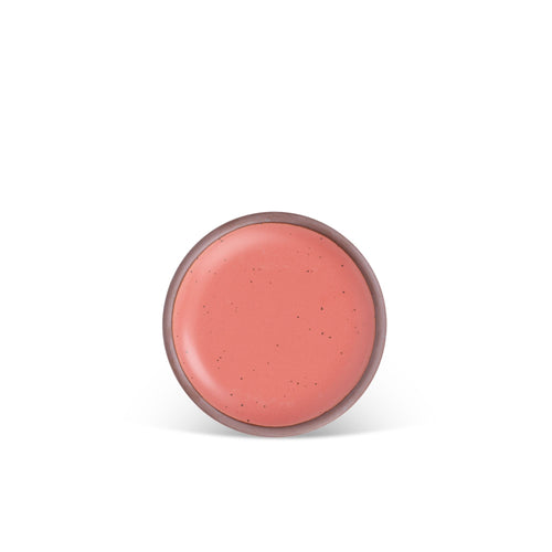 A dessert sized ceramic plate in a watermelon pink color featuring iron speckles and an unglazed rim.