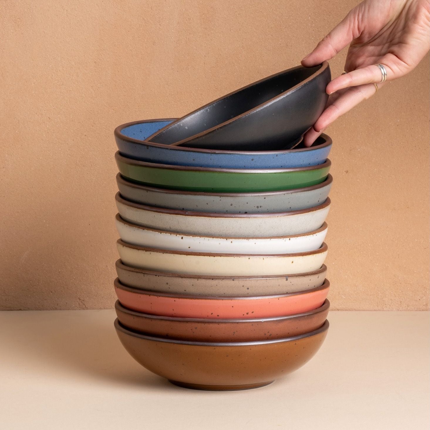 A hand places a bowl on a tall stack of rainbow shallow dinner bowls
