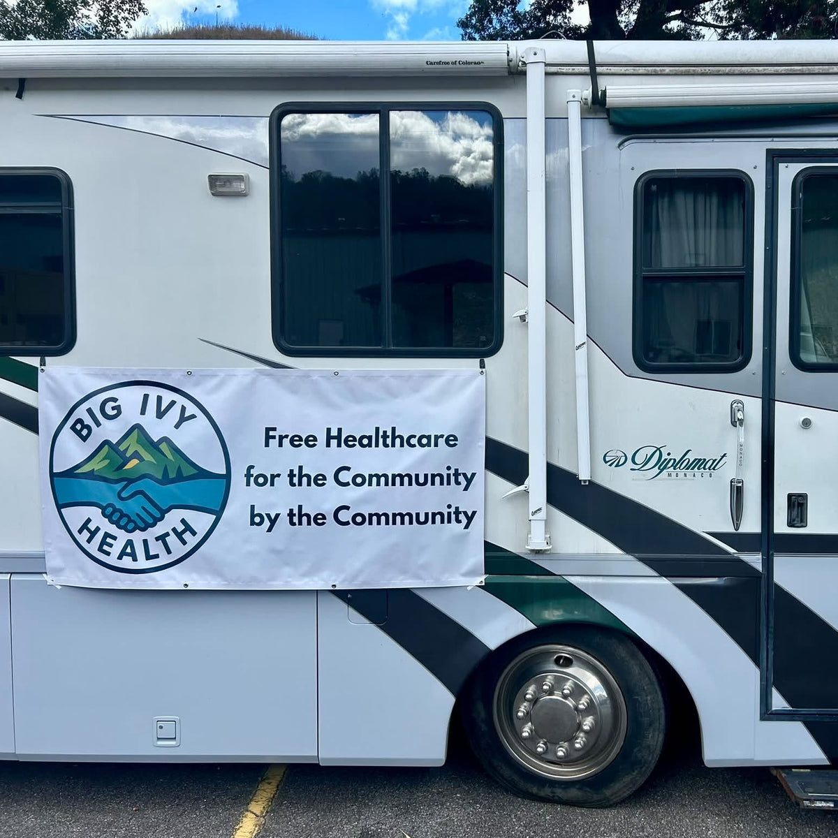 An RV with a banner on its side that reads 'Blue Ivy Health Free Healhcare for the Community by the Community'