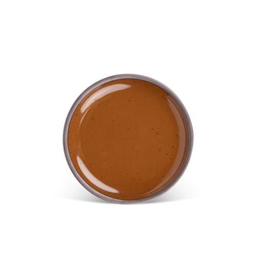 A medium sized ceramic plate in a glossy caramel brown color featuring iron speckles and an unglazed rim.