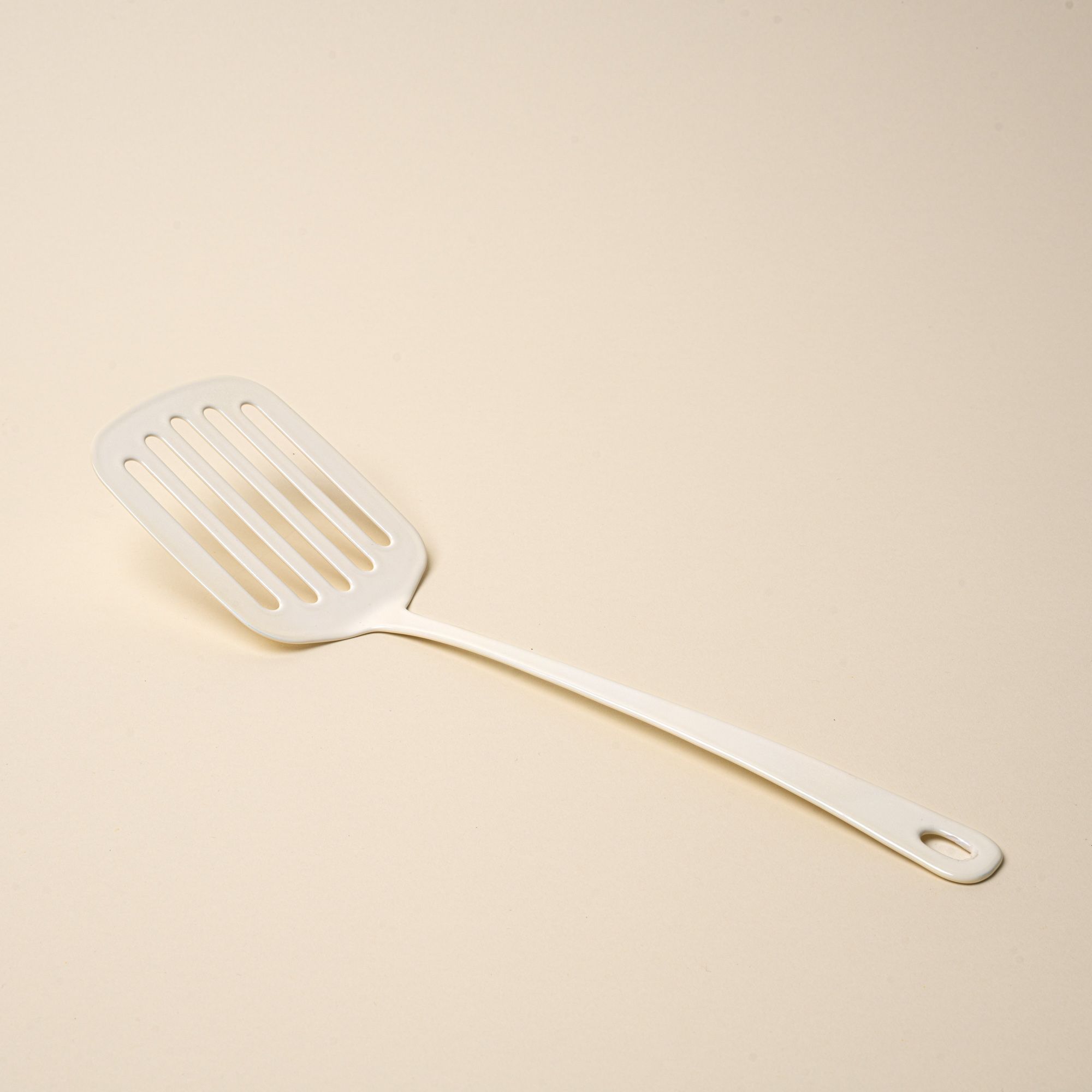 A white enamel spatula with a hole at the end of the handle for hanging.