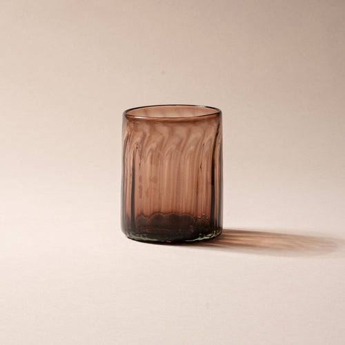 Taller amber-brown glass tumbler with vertical ridges, set against a neutral background.