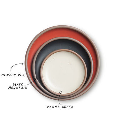 A stack of 3 plates in Dinner, Side, and Cake sizes in a bold red, graphite black, and warm off-white colors.