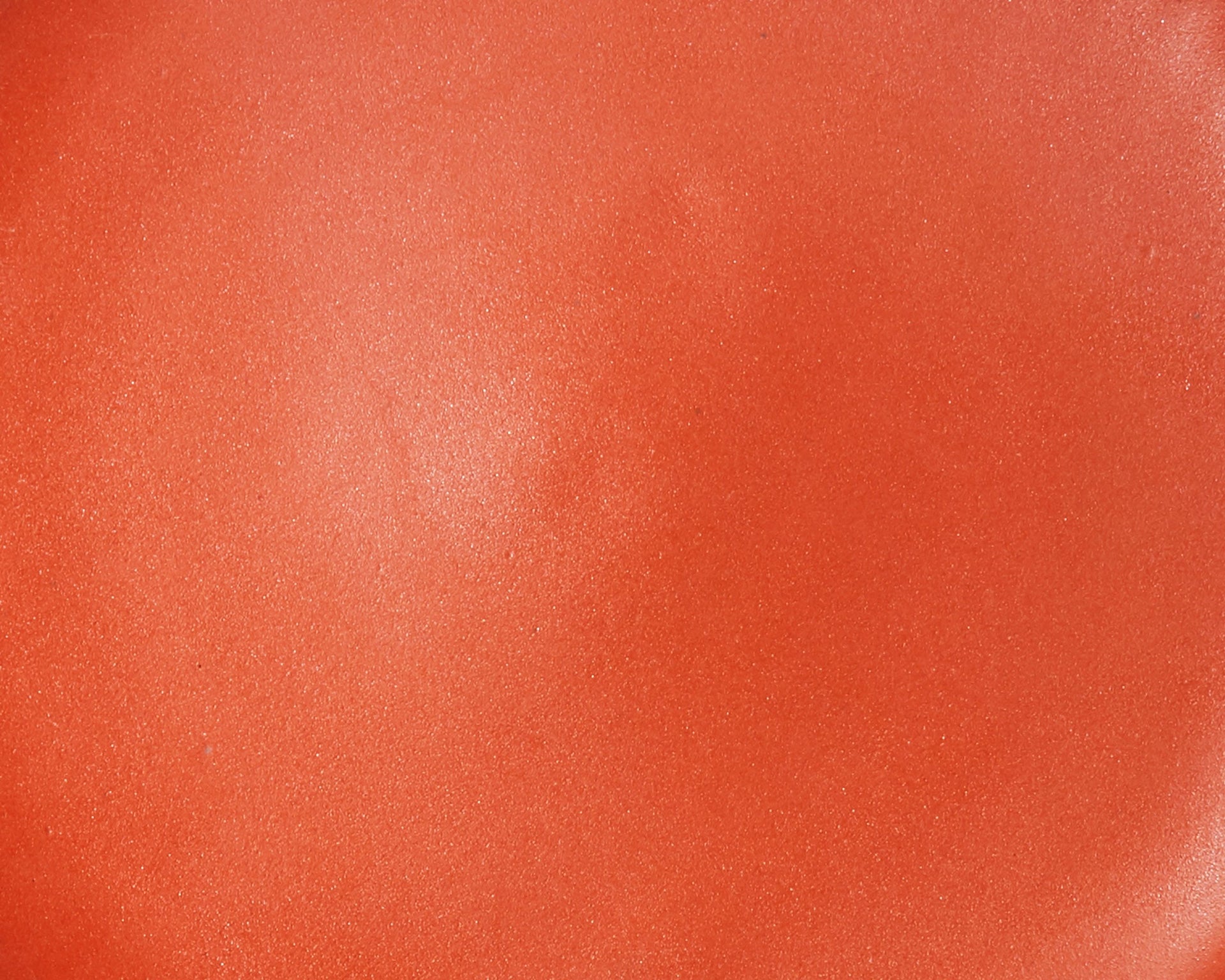 A closeup of a ceramic plate in a fiery orange color with a few subtle iron speckles throughout
