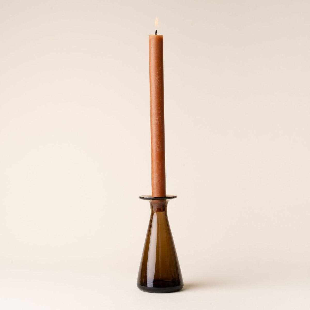 Amber glass candlestick holder with a lit brown taper candle, styled against a neutral backdrop.