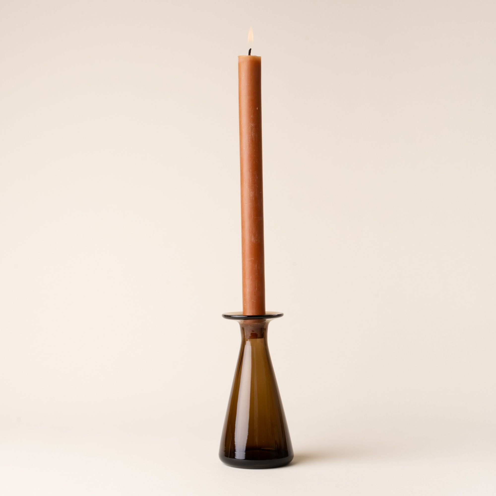 Amber glass candlestick holder with a lit brown taper candle, styled against a neutral backdrop.