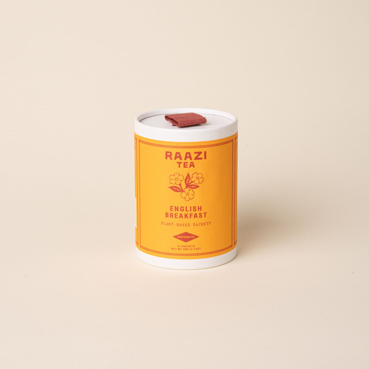 A white cylindrical tin of RAAZI Tea labeled ‘English Breakfast’ with an orange label and small red pull tab, photographed on a pale beige background.