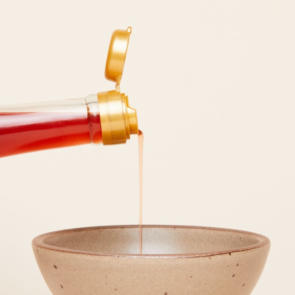 Purple sweet potato vinegar streams from a bottle into a brown bowl