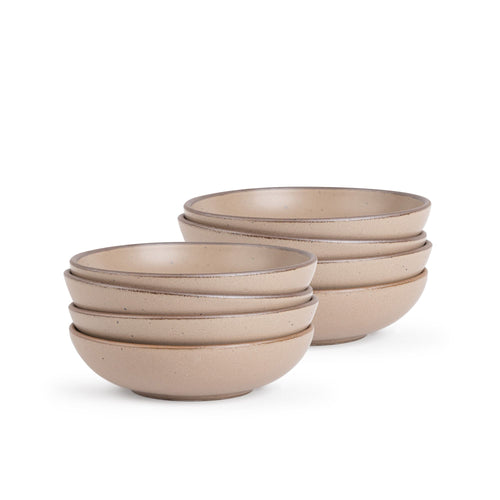 A stack of 8 dinner-sized shallow ceramic bowls in a warm pale brown color featuring iron speckles and an unglazed rim