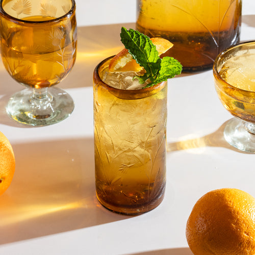 Amber etched glass tumbler filled with ice, lemon slices, and mint leaf with matching glassware.