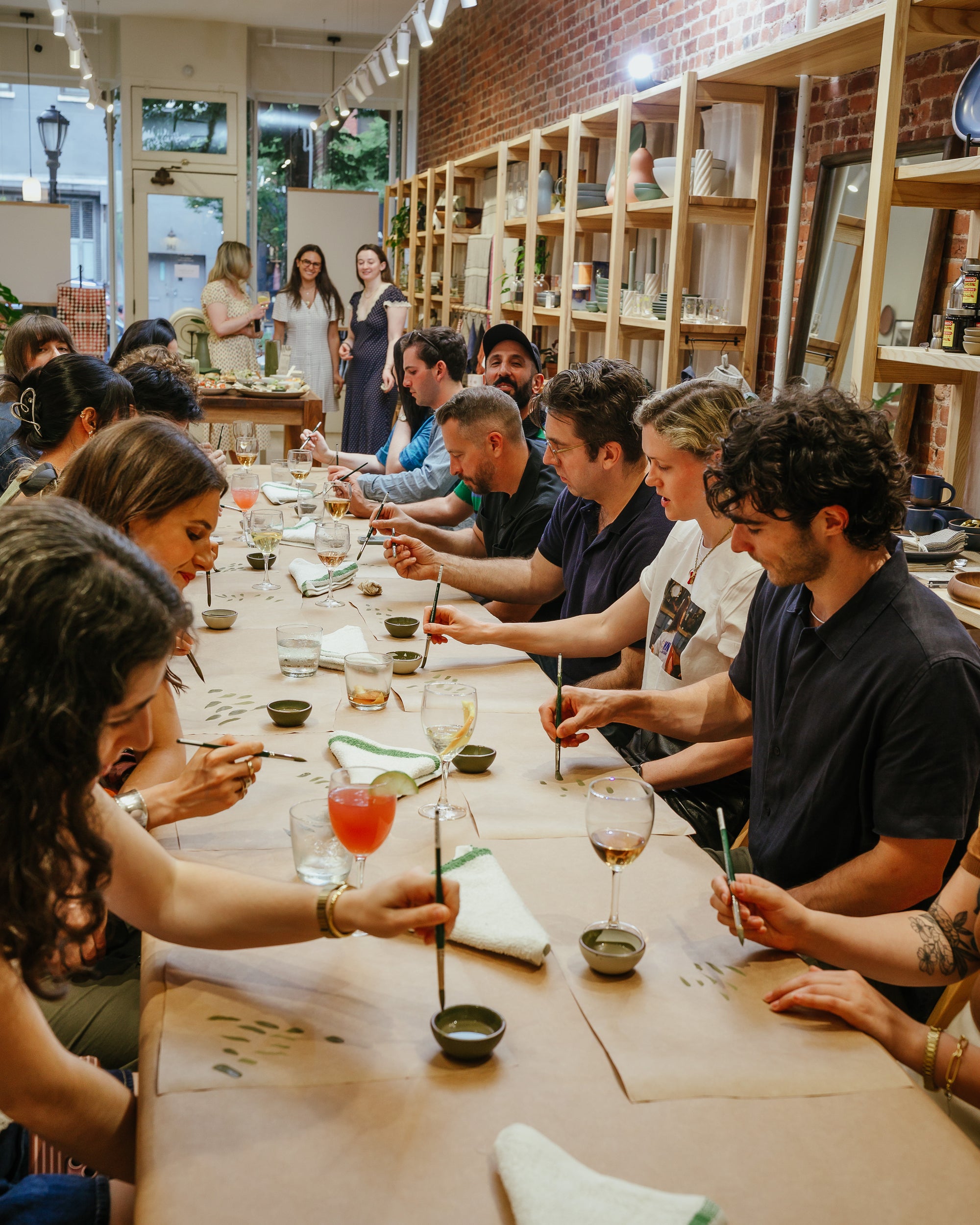 Group of people sitting around a long table in East Fork Brooklyn, practicing painting.