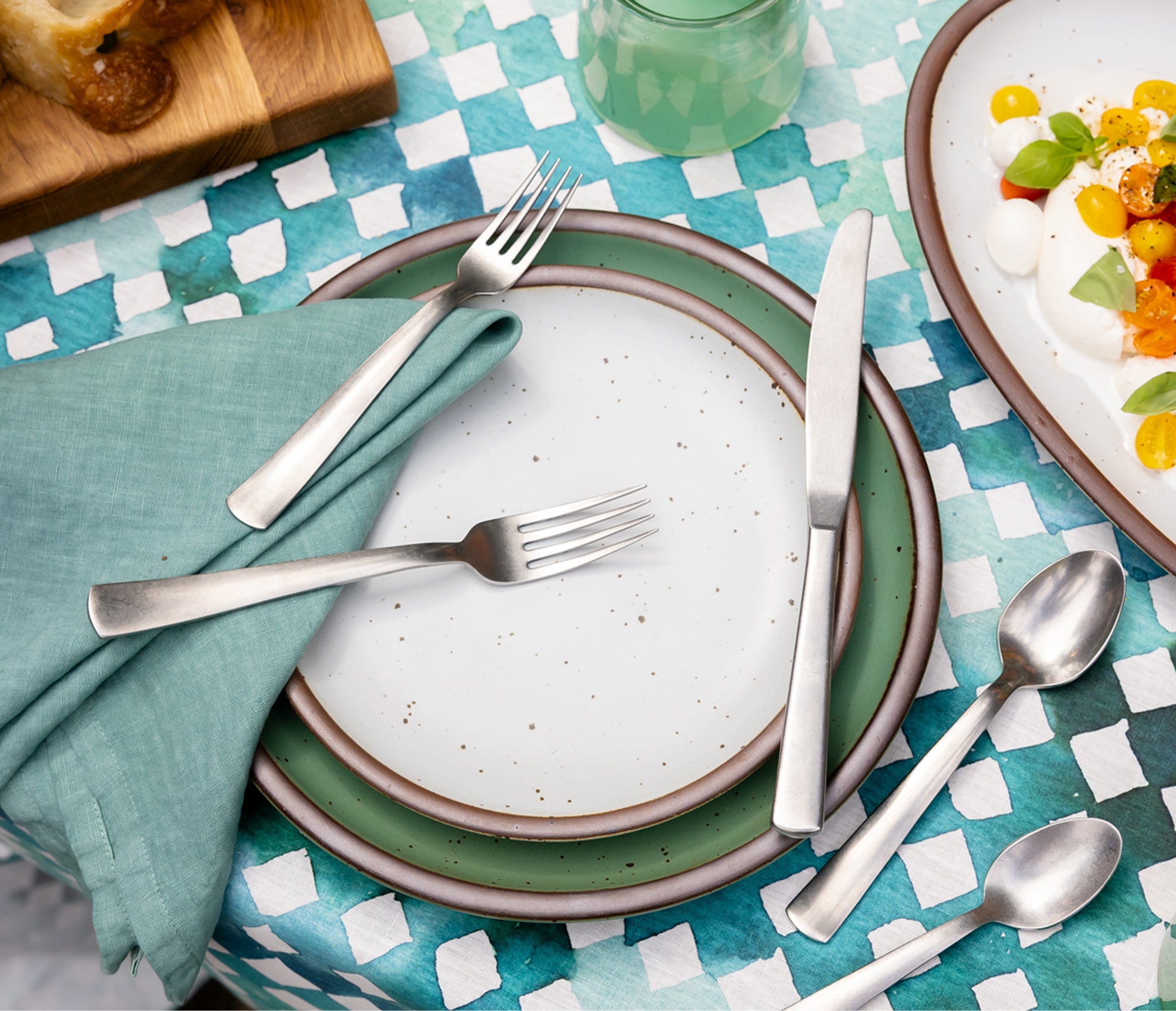 Dining table setting with ceramic  plates, cutlery, and a green checkered tablecloth.