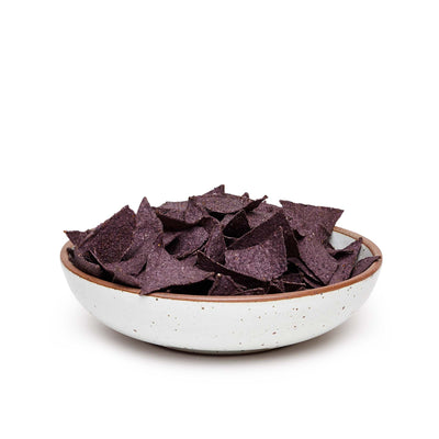 A large shallow serving ceramic bowl in a cool white color featuring iron speckles and an unglazed rim, filled with tortilla chips