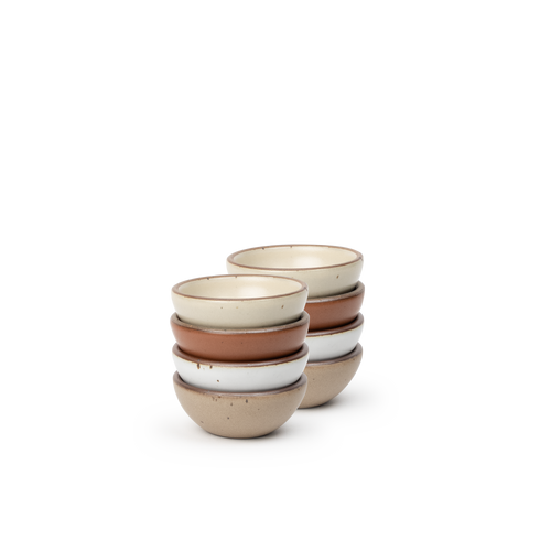 A stack of 8 tiny rounded ceramic bowls in a cool terracotta, warm off-white, cool white, and warm pale brown colors featuring iron speckles and an unglazed rim