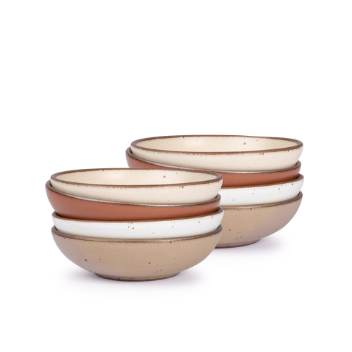 A stack of 8 dinner-sized shallow ceramic bowls in a warm off-white, cool terracotta, cool white, and pale warm brown colors featuring iron speckles and an unglazed rim