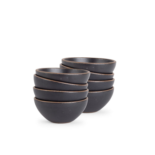 A stack of 8 small dessert sized rounded ceramic bowls in a graphite black color featuring iron speckles and an unglazed rim