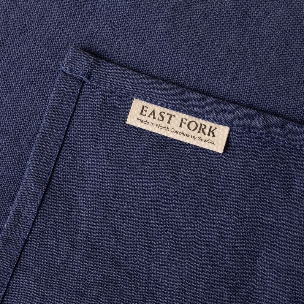 A muted blue linen napkin close up of texture and sewn-in corner tag that reads "East Fork"