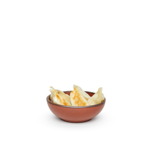Dumplings in a small shallow ceramic bowl in a cool burnt terracotta color featuring iron speckles and an unglazed rim