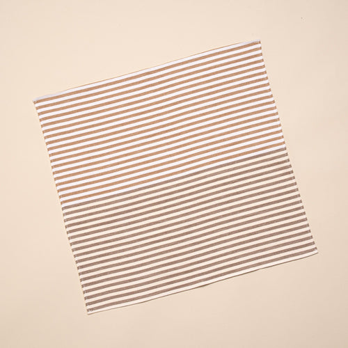 A square cloth with horizontal brown and white stripes is laid flat against a light beige background.