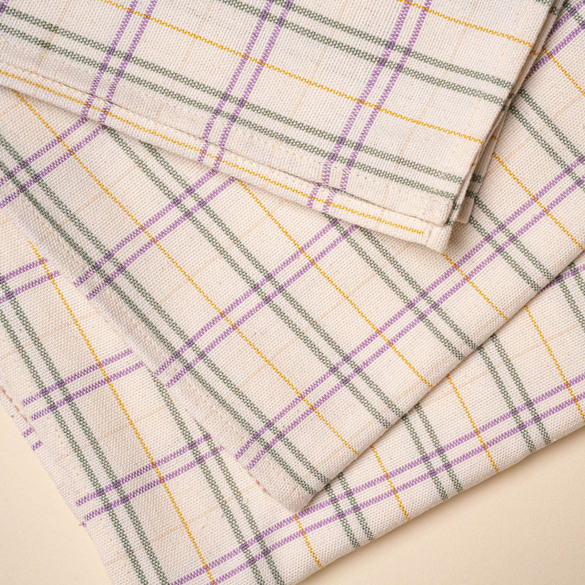 A closeup of a plaid tablecloth with lines of purple, yellow, and dark teal.