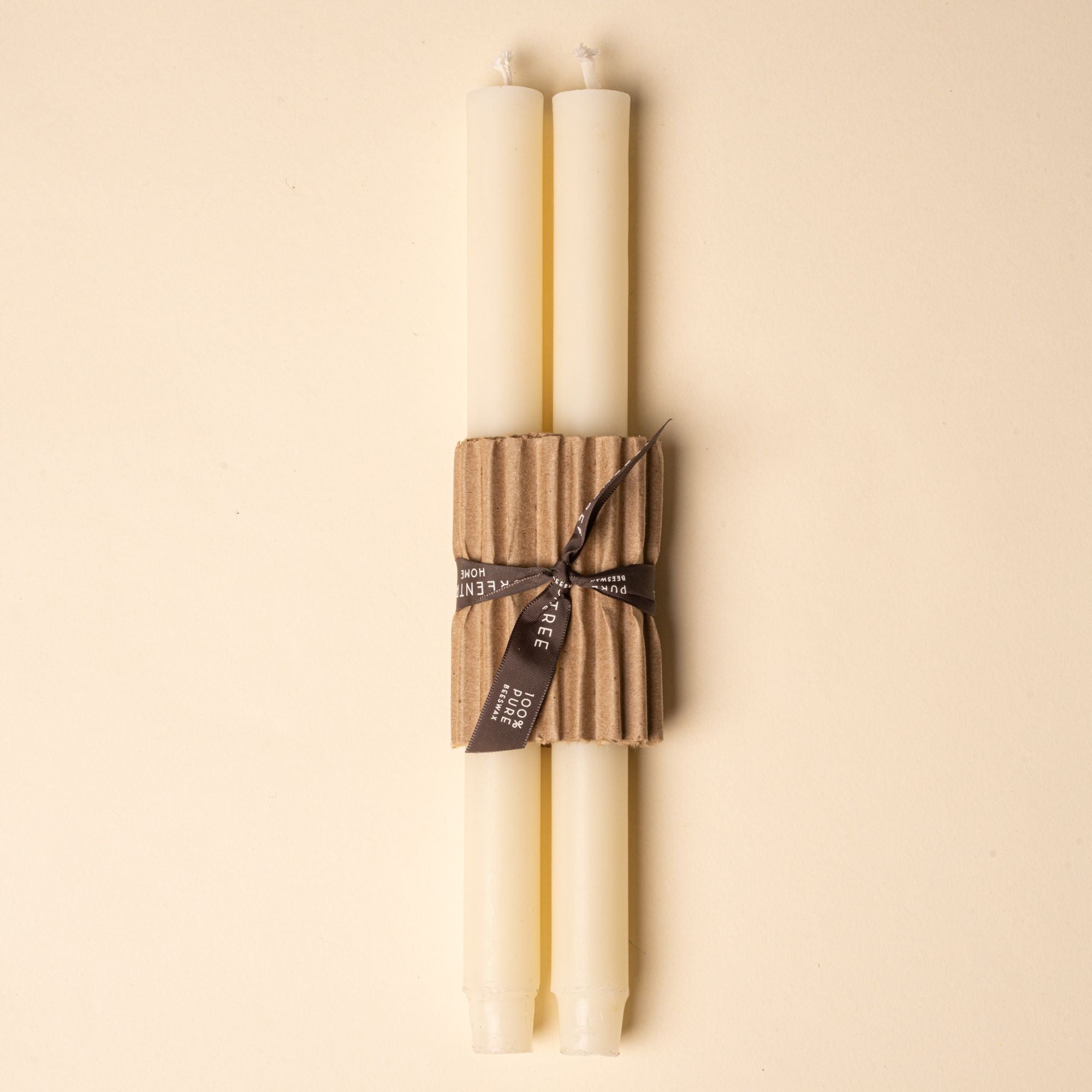 Two ivory taper candles bundled with corrugated cardboard and tied with a black ribbon on a neutral background.