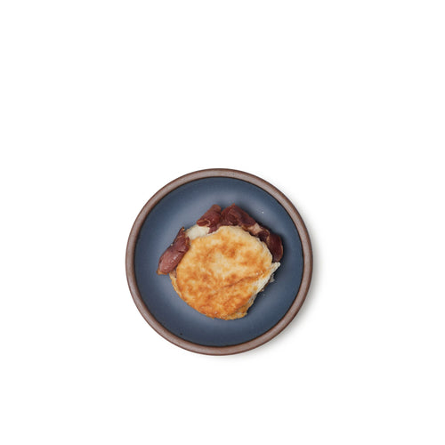 A breakfast sandwich on a dessert sized ceramic plate in a cool medium blue color featuring iron speckles and an unglazed rim.