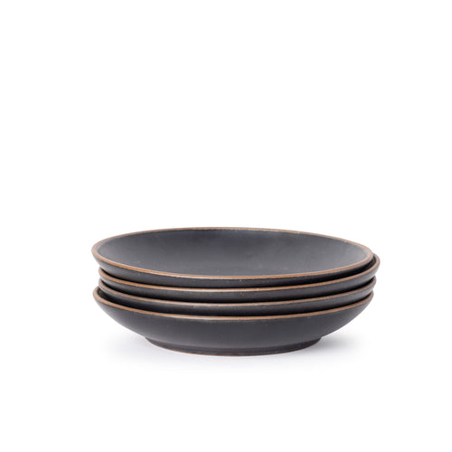 A stack of 4 large ceramic plates with a curved bowl edge in a graphite black color featuring iron speckles and an unglazed rim.