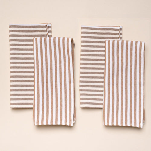 Four folded cotton napkins with brown and white vertical and horizontal stripes, arranged on a neutral background.