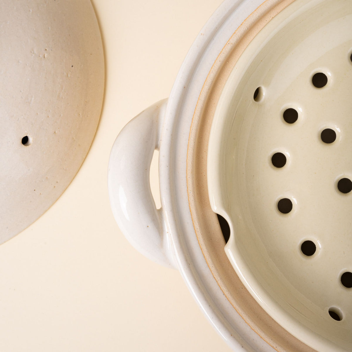 An overhead view of a ceramic white donabe steamer focusing on the steamer tray inside.