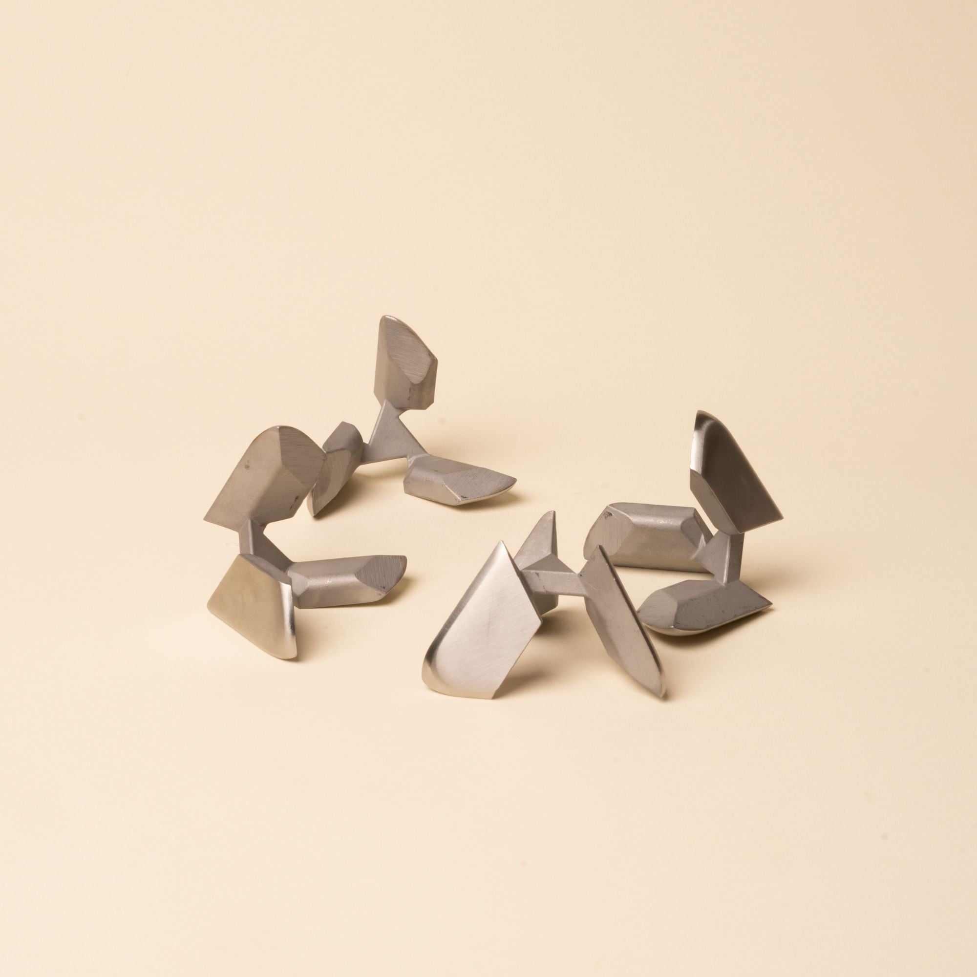 Disassembled silver metal tetra puzzle pieces arranged loosely on a neutral surface.