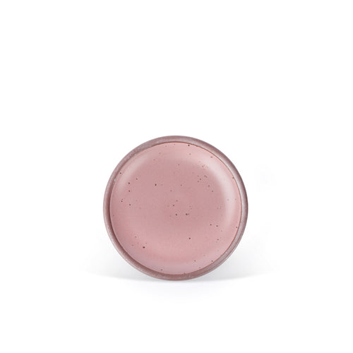 A dessert sized ceramic plate in a dusty mauve pink color featuring iron speckles and an unglazed rim.