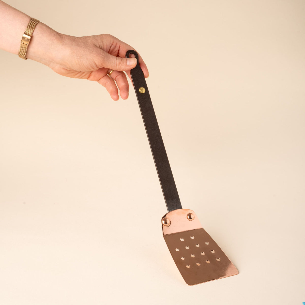 A hand holds up a copper spatula with a black iron handle