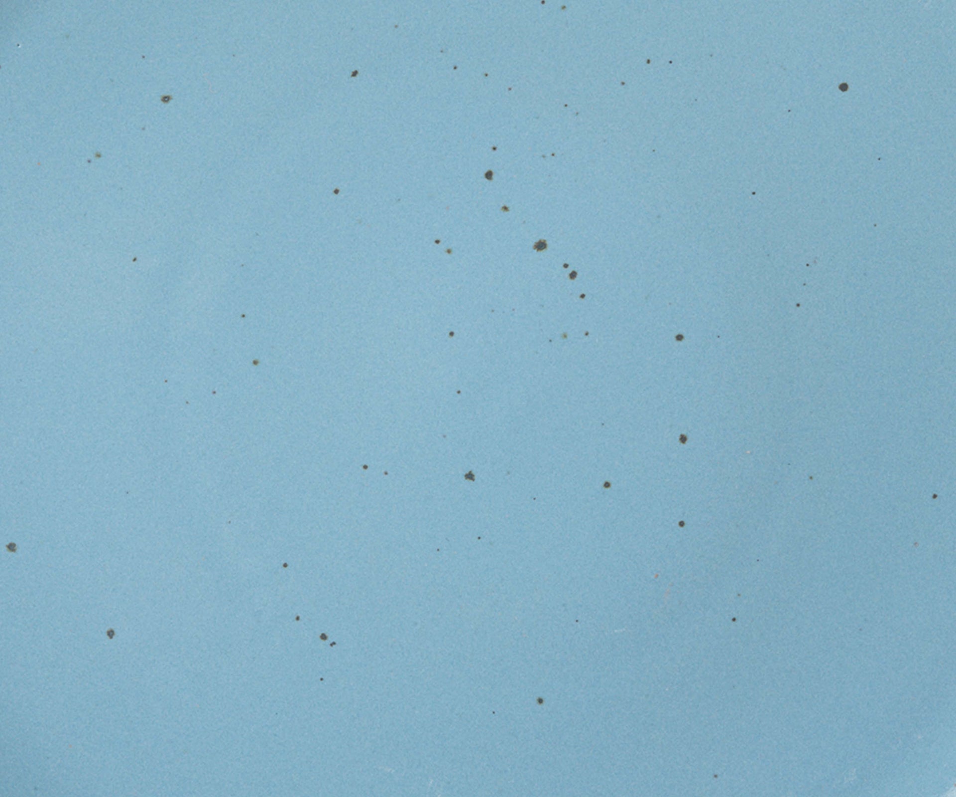 A closeup of a ceramic plate in a glossy cerulean color with iron speckles throughout