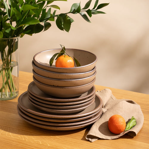 4 ceramic dinner plates, 4 side plates, and 4 shallow dinner bowls in a warm pale brown color with iron speckles and unglazed rims are stacked all together on a table with oranges.