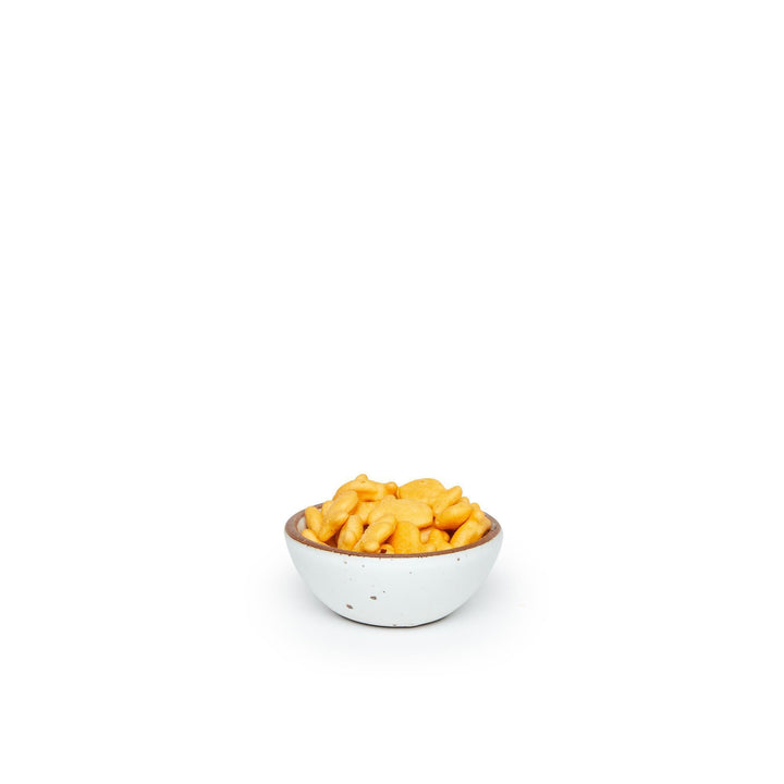 A tiny rounded ceramic bowl in a cool white color featuring iron speckles and an unglazed rim, filled with crackers