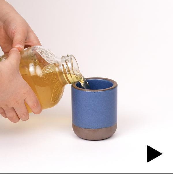 Video of a hand placing a tiny cup in a cool blue while a child's hands pour apple juice into the cup until it spills over