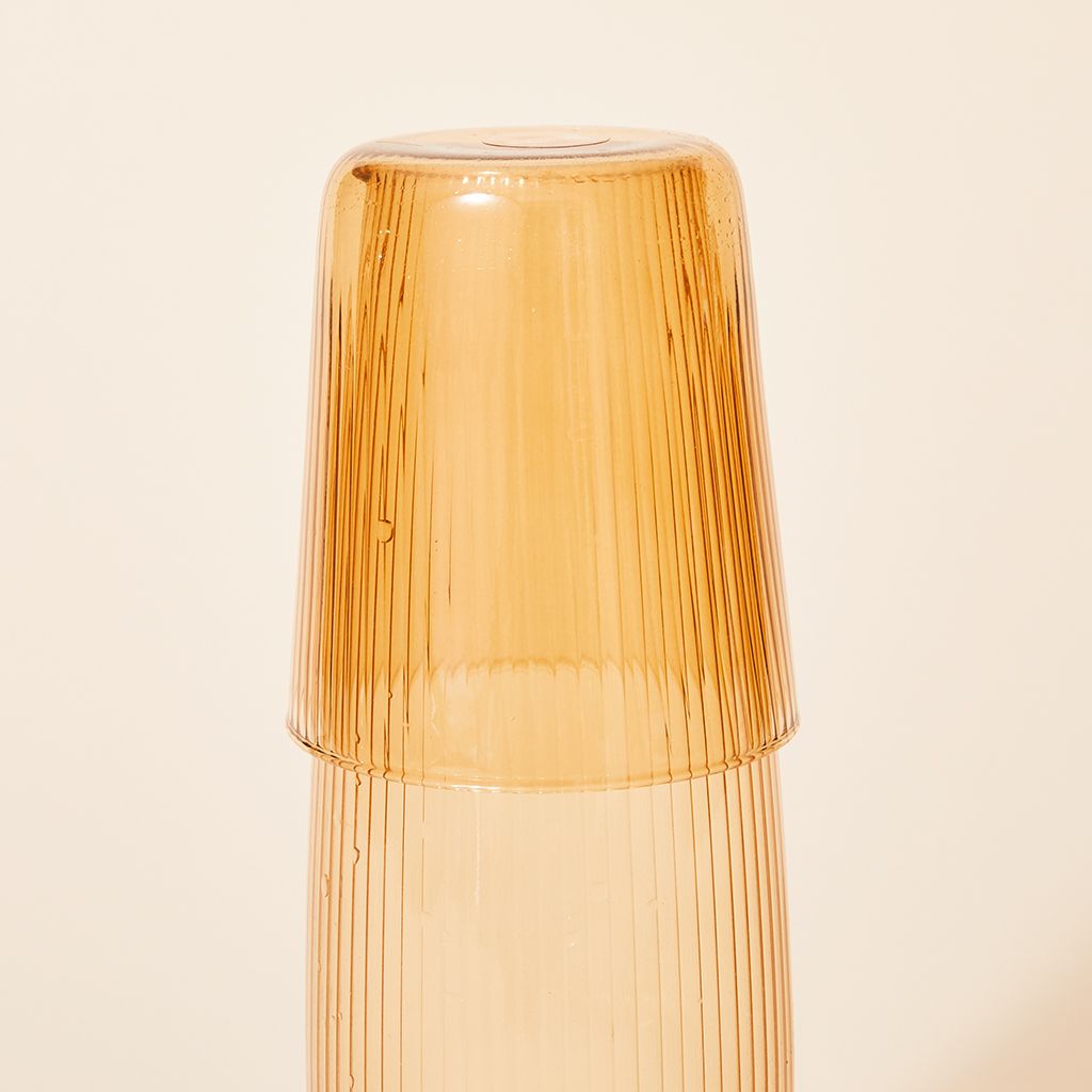 A yellow drinking glass is upside down, covering the top of a tall, pale yellow pitcher