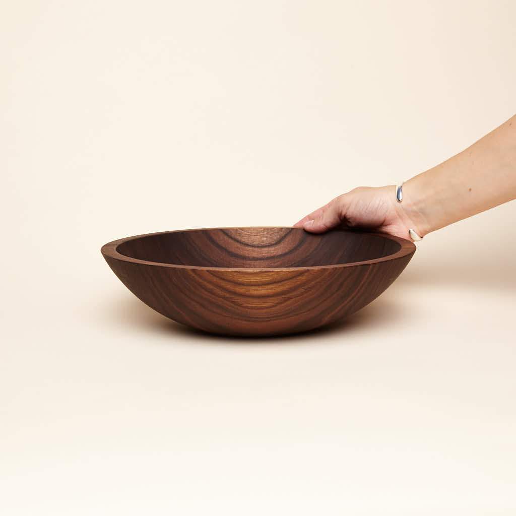 A hand is placed on a medium-sized shallow walnut wood bowl