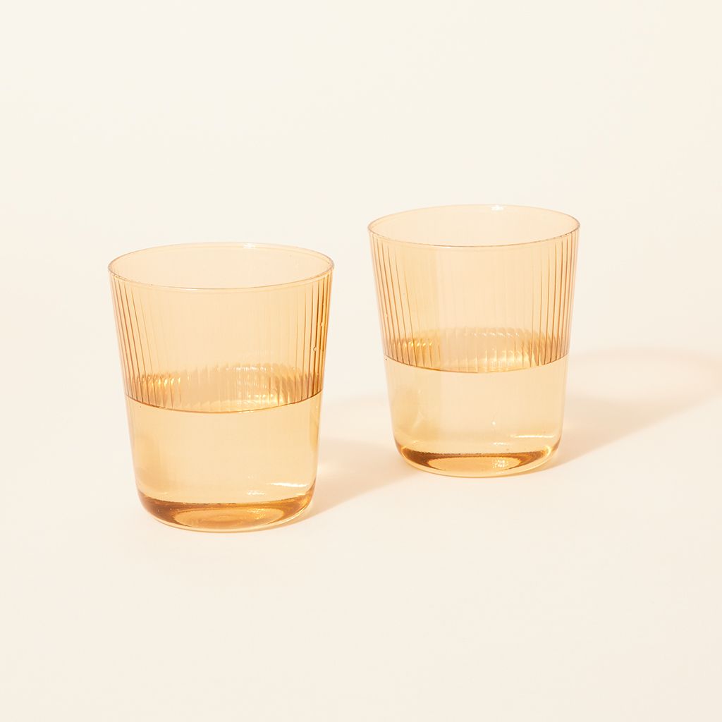A pair of clear pale yellow drinking glasses that are half full of water