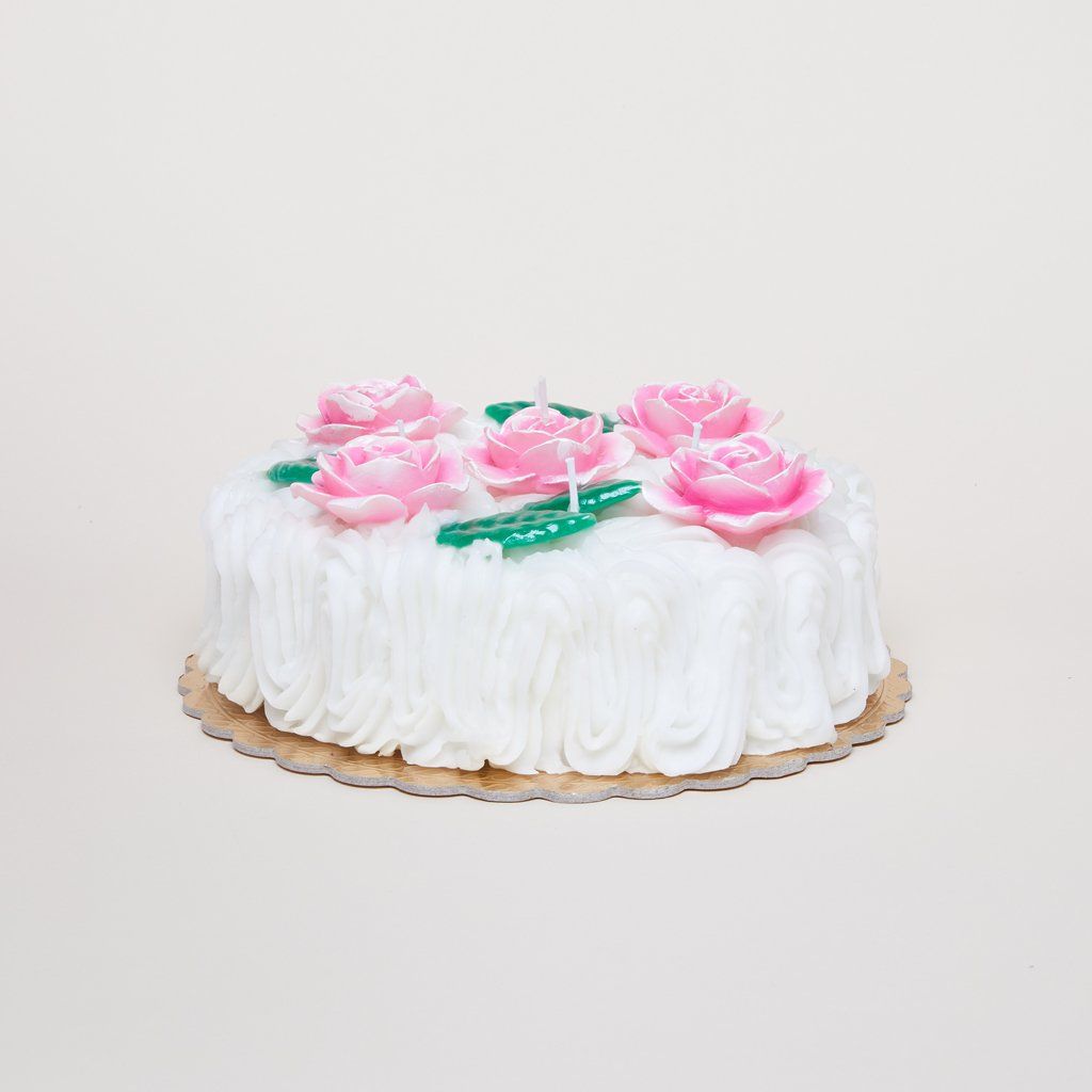 A round candle made to mimic a cake with thick white icing and pink roses