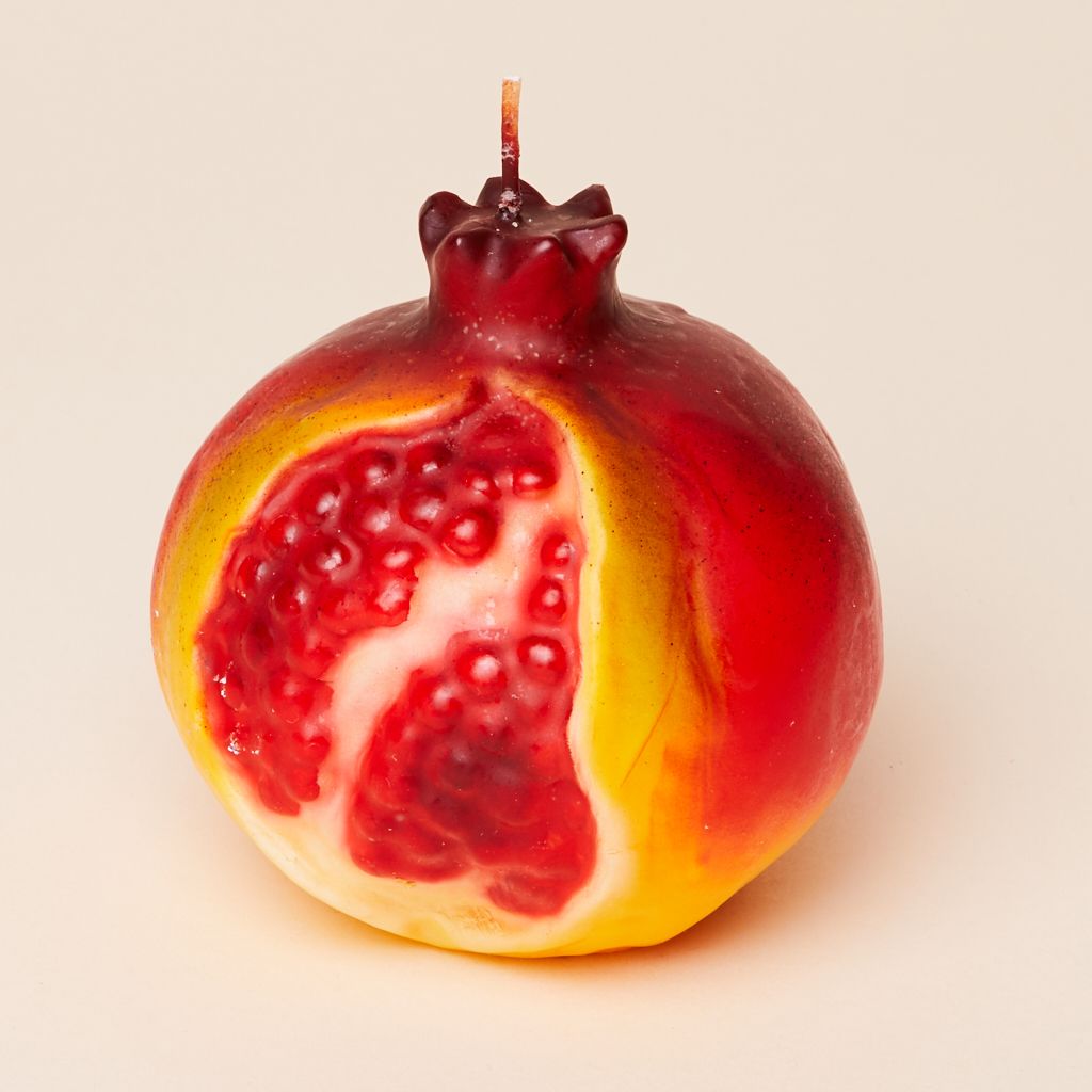 A round candle that is red, white and yellow, to suggest a pomegranate with a cut in its side